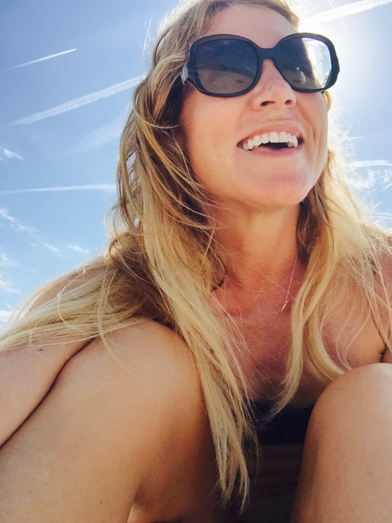 Blond woman in sunglasses with the sun's rays behind her.